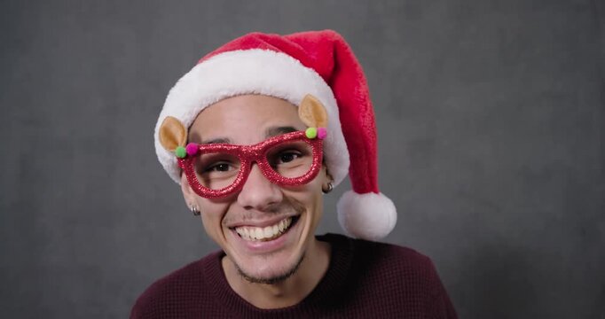 Adult African American man glancing, fixing glasses, tugging Santa hat tail in studio, showing joy