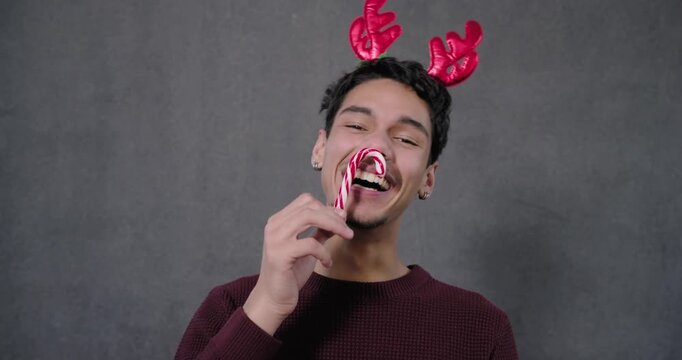 African American adult male holding candy cane near face, tapping antler headband, celebrating