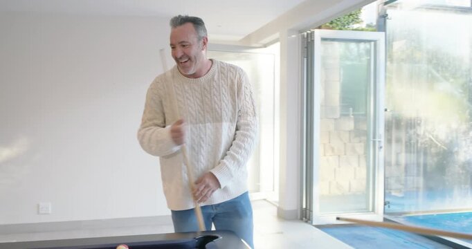 Diverse male friends playing pool in game room, cream-sweater entering, gray taking shot for fun