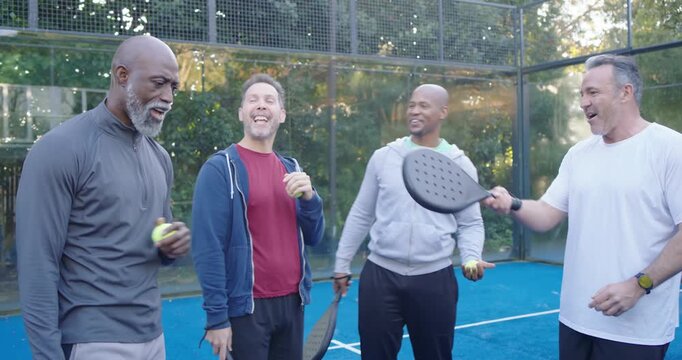 Diverse male friends chatting, passing yellow balls with paddles on blue court huddling before play