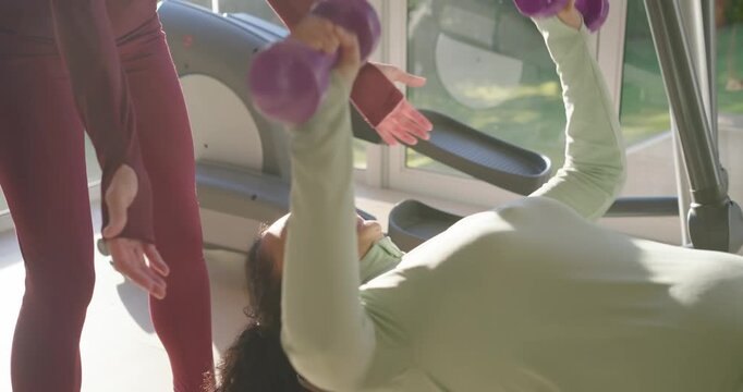Lifter is settling on bench holding dumbbells, doing chest presses for strength while spotter aids