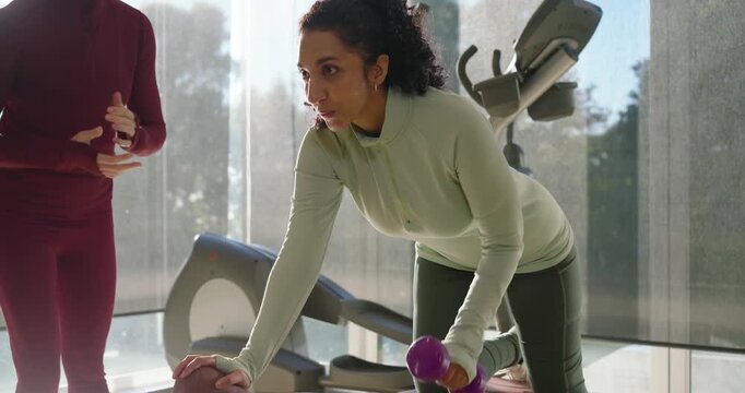 African American trainee doing single-arm rows with purple dumbbell on bench while trainer counting