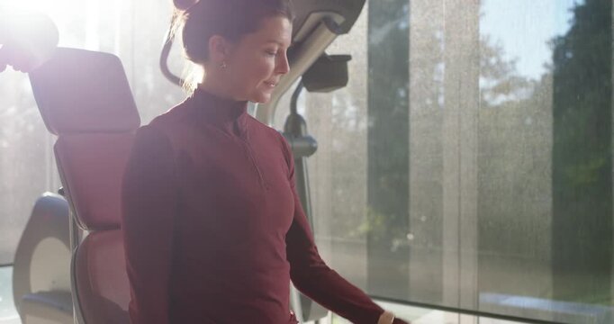 Woman sitting on bench reaching silver dumbbell, curling right arm in home gym, building strength