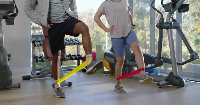 Diverse friends starting ankle band warm-up, performing alternating leg lifts in home gym
