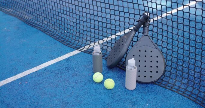 Padel paddles, tennis balls, bottles are staying propped near net as camera is panning showing gear