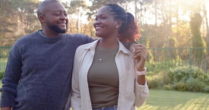 African couple standing in garden man draping arm sharing smiles woman leaning in posing for camera