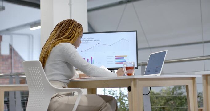 Diverse team African woman reading report on screen at desk pointing and speaking as peer passing