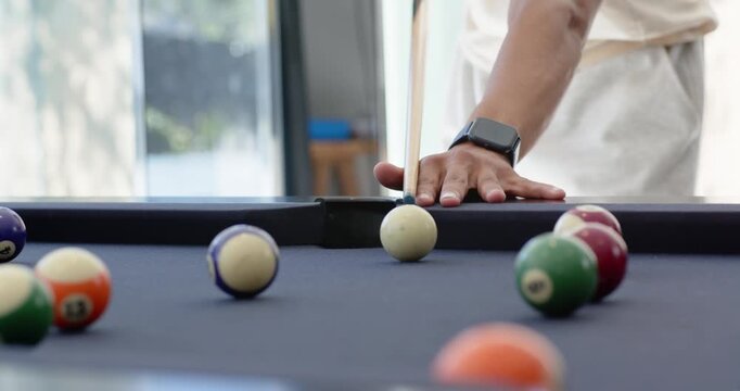 Adult African man leaning over pool table at home lining shot striking cue pocketing orange ball