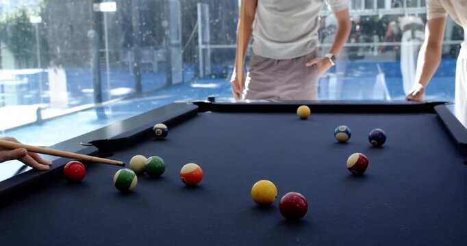 Diverse men taking turns lining and striking cue on lounge pool table with balls for fun