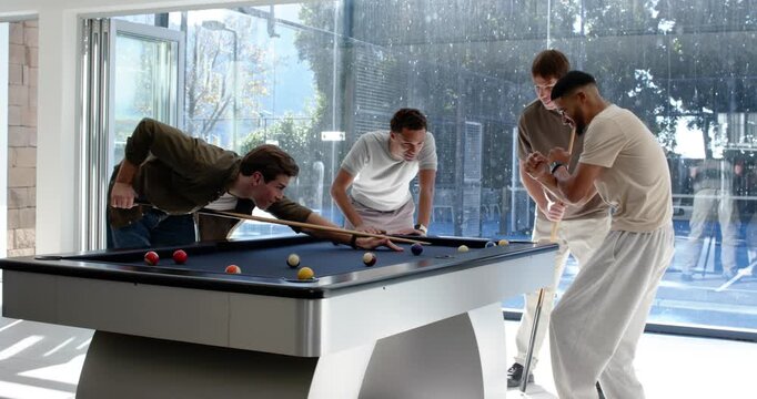 Diverse male friends watching player lining and taking shot on blue pool table during casual game