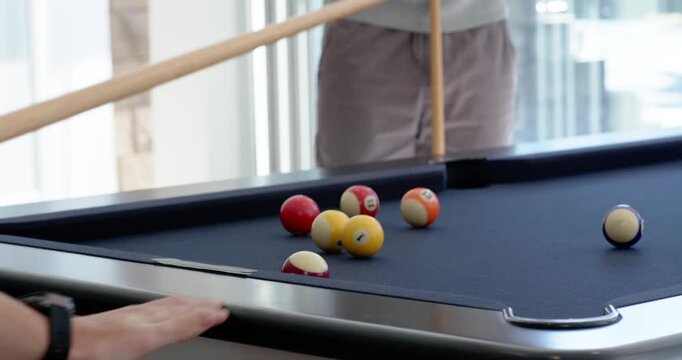 Diverse male friends at home, player drawing then striking cue ball, wristband, orange pocketing