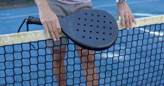 African American man placing paddle atop net holding yellow ball, pausing after play on blue court