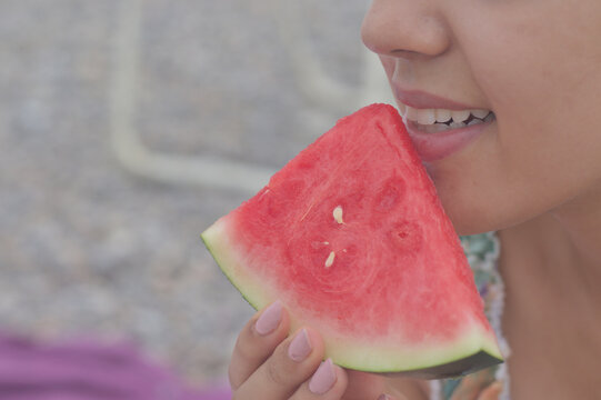 A woman's hand picking up a piece of watermelon while enjoying a day at the beach