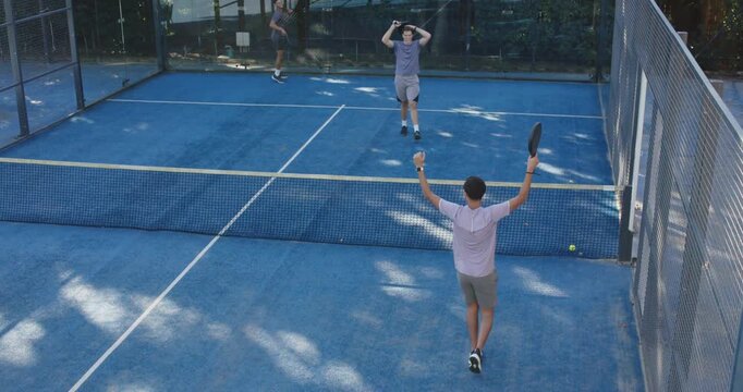 Four men on blue padel court celebrating point, ball landing near net, raising paddles and hugging
