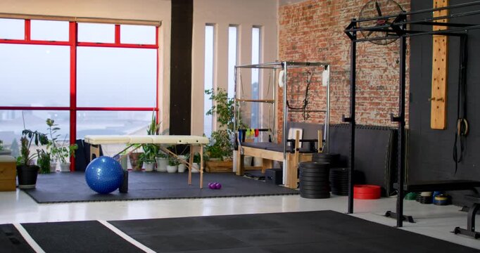 Camera is shifting rightward to reveal rig and weights beside massage table and blue ball
