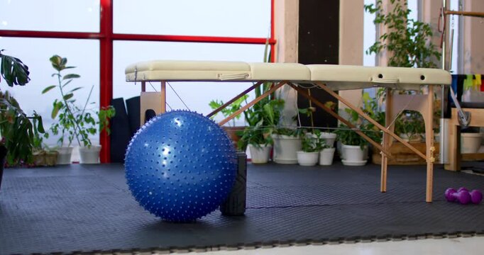 Camera is widening, revealing blue spiky exercise ball shifting left and settling near foam roller