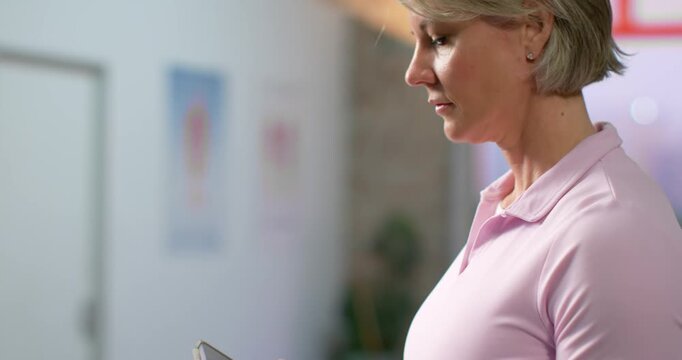 Senior woman in pink polo holding smartphone after alert, scrolling on screen in clinic, copy space