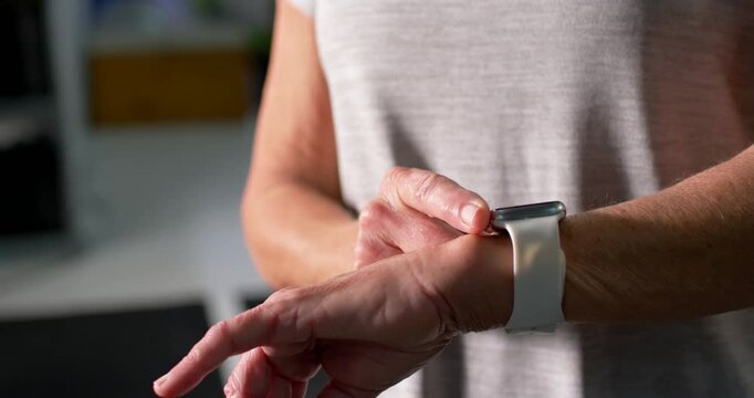 Senior woman tapping white band smartwatch post-set, checking stats, showing smiling face at gym