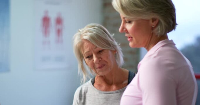 Female trainer in pink polo and client in clinic checking clipboard while trainer explaining plan