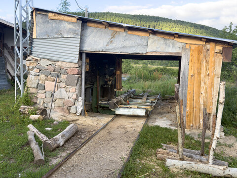 View of a rustic sawmill with a stone and wood structure, metal roof, and log processing tracks in a rural setting in Posof, Ardahan, Turkiye.