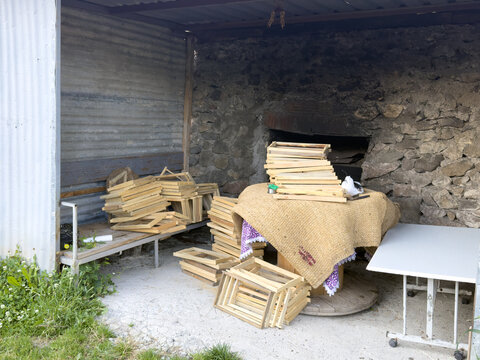 View of wooden beehive frames stacked in a rustic outdoor workspace with stone walls and corrugated metal siding in Posof, Ardahan, Turkiye.