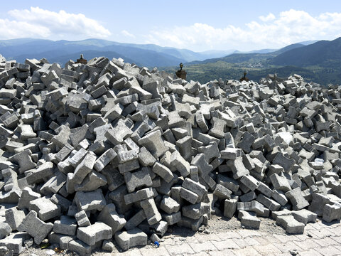 View of a large pile of grey interlocking concrete paving stones stacked outdoors against a backdrop of rolling mountains and a blue sky in Posof, Ardahan, Turkiye.