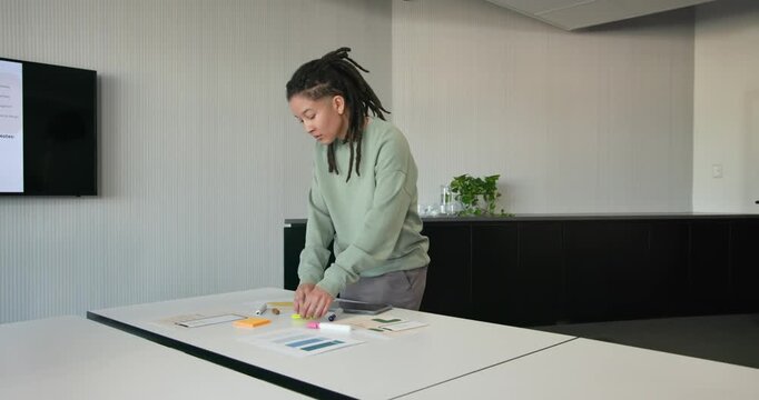Nonbinary African American reading sticky note arranging neon pads and tablet at table preparing