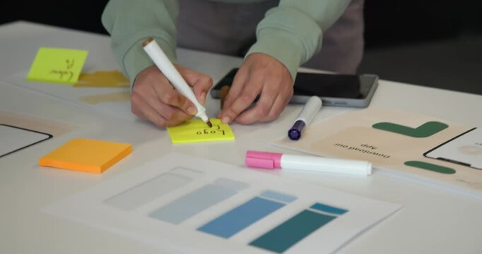African nonbinary person writing Logo on yellow note arranging swatches in meeting room planning