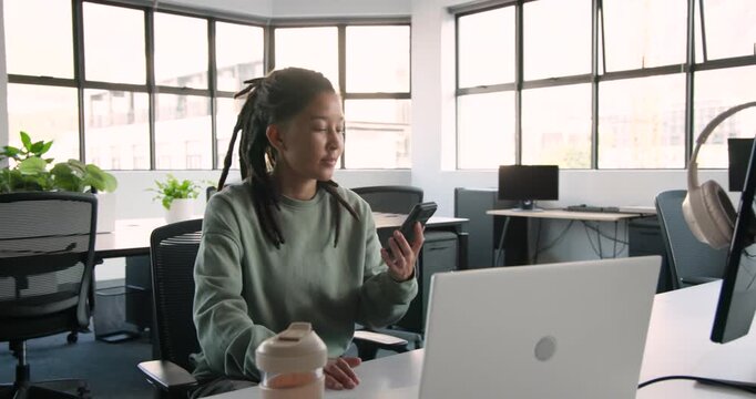 African American nonbinary in green sweatshirt answering incoming call at desk, pacing by laptop