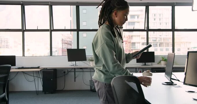 African non-binary person entering office reading tablet sipping cup typing on laptop starting work