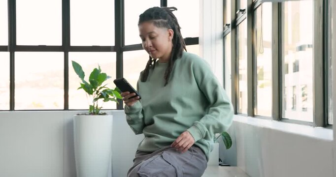 Non-binary person walking into office corner, checking smartphone, sitting on bench and smiling