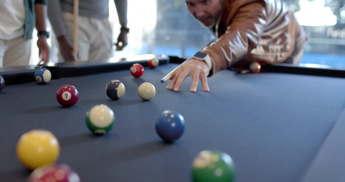 Diverse men watching shooter lining up, hitting balls with cue during game on blue-felt table