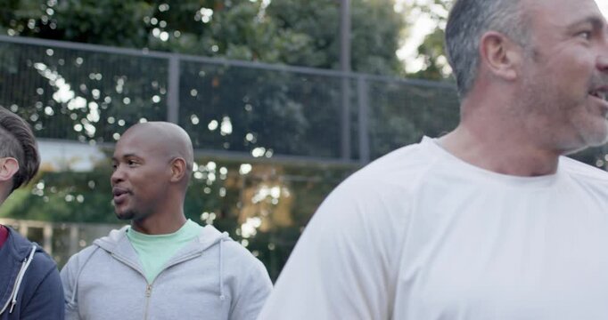 Diverse four men watching gray-hoodie man tossing tennis balls, tracking ball for practice on court
