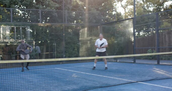 Male doubles reacting to lob on blue paddle court, light-grey-hoodie swinging paddle returning shot