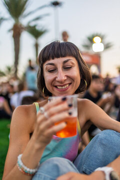 The young woman celebrates at a summer open party, raising a glass with friends. summer festival. girl with cocktail outside.