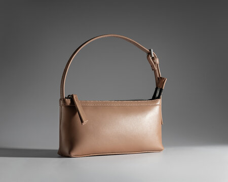 Minimalist light brown leather baguette shoulder bag on plain grey background