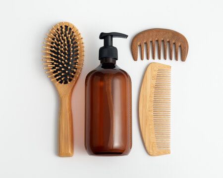 Amber glass dispenser bottle with wooden hair brush and combs on white background