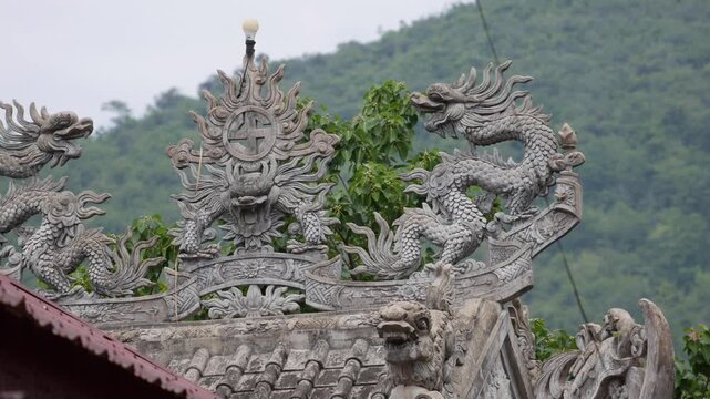 Stone dragon ornaments and a decorative roof ridge on a buddhist pagoda with green mountains behind. Sacred ornamentation.