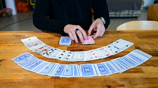Playing with cards. Person performing a card flourish on a wooden table. Open fan of playing cards displayed on a wooden surface. Magician spreading playing cards for a trick. 