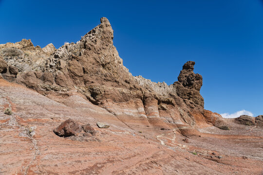 View of the volcanic landscape of Mount Teide with rugged rock formations and reddish terrain under a clear blue sky in Santa Cruz de Tenerife, Canary Islands, Spain.