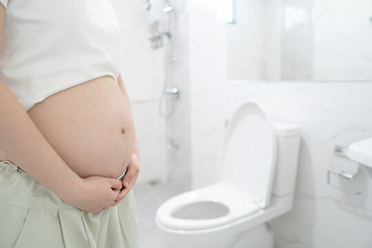 Incontinence and frequent urination during pregnancy. Pregnant woman need to pee standing by toilet in bathroom.