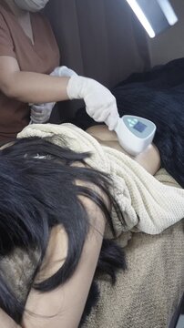 Female patient receiving radiofrequency back contouring treatment at an aesthetic clinic for skin tightening and fat reduction