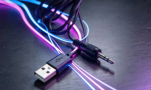 Neon illuminated audio jack and USB cable on dark surface