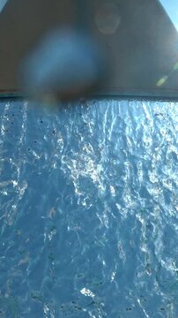 Water cascading from hydromassage waterfall spout at outdoor water park against blue sky
