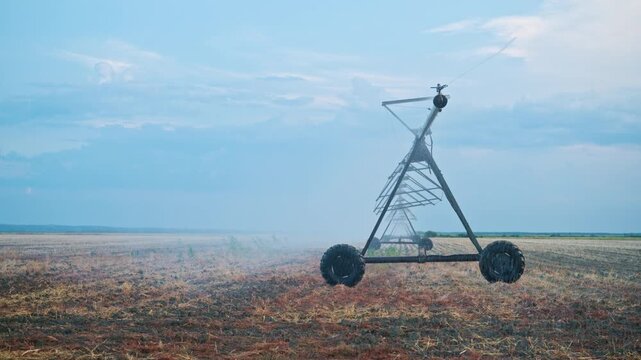 Large center pivot irrigation machine positioned across parched farmland during the evening. Agricultural technology, crop irrigation, water conservation and sustainable farming, 4K.