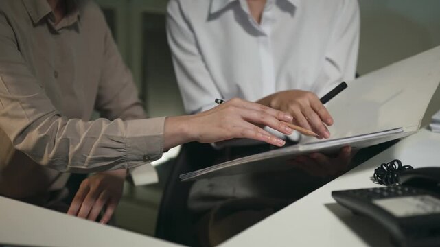 Closeup Two Businesswomen Consulting Over Documents at Office Desk During Late Night Work Session