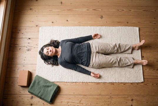 High angle view of a mature woman practicing yoga in corpse pose shavasana on a rug over wooden floor at home