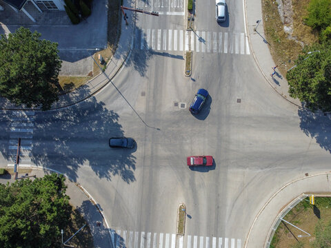 Vehicles navigating through an urban intersection from an aerial drone view. Aerial drone shot of cars driving through a city intersection.