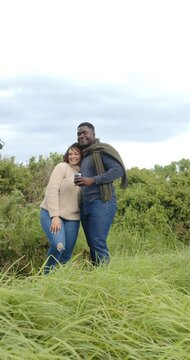 Vertical video: Wind pushing African American couple seeking warmth on hill man holding cup scarf