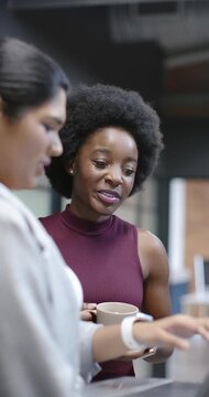 Vertical video: Diverse women at counter left tapping laptop center watching and speaking with mug